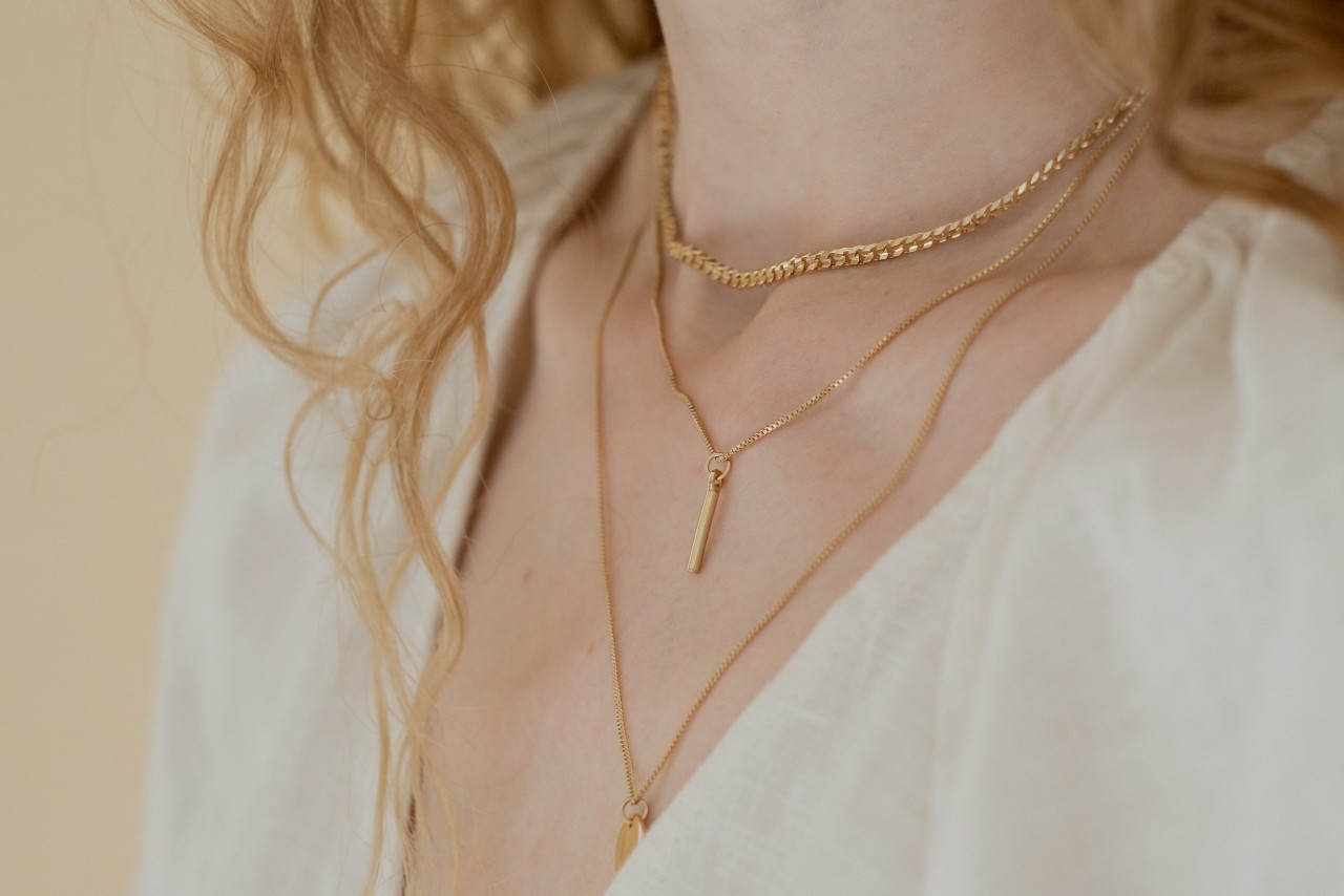 A close-up of a woman’s neck and decolletage, adorned with delicate layers of yellow gold necklaces. A close-up of a woman’s neck and decolletage, adorned with delicate layers of yellow gold necklaces.
