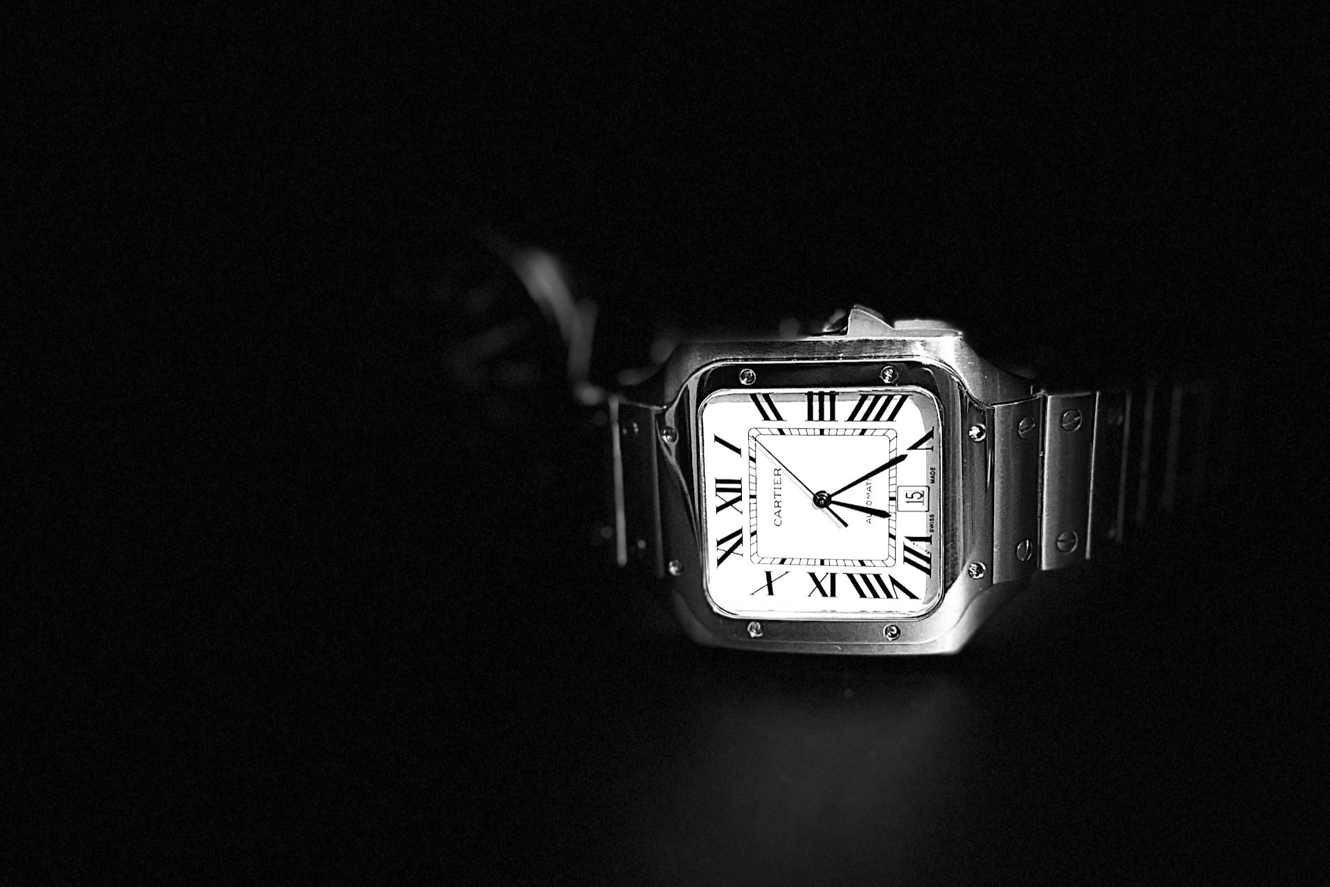 a black and white photo of a Cartier Santos watch on a black background