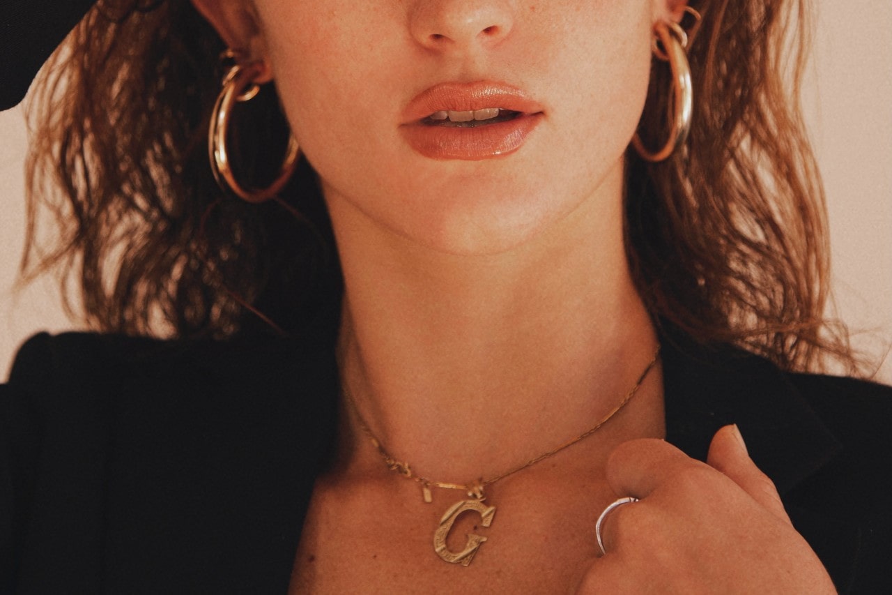 A woman wearing large gold hoop earrings and a gold “G” initial necklace.