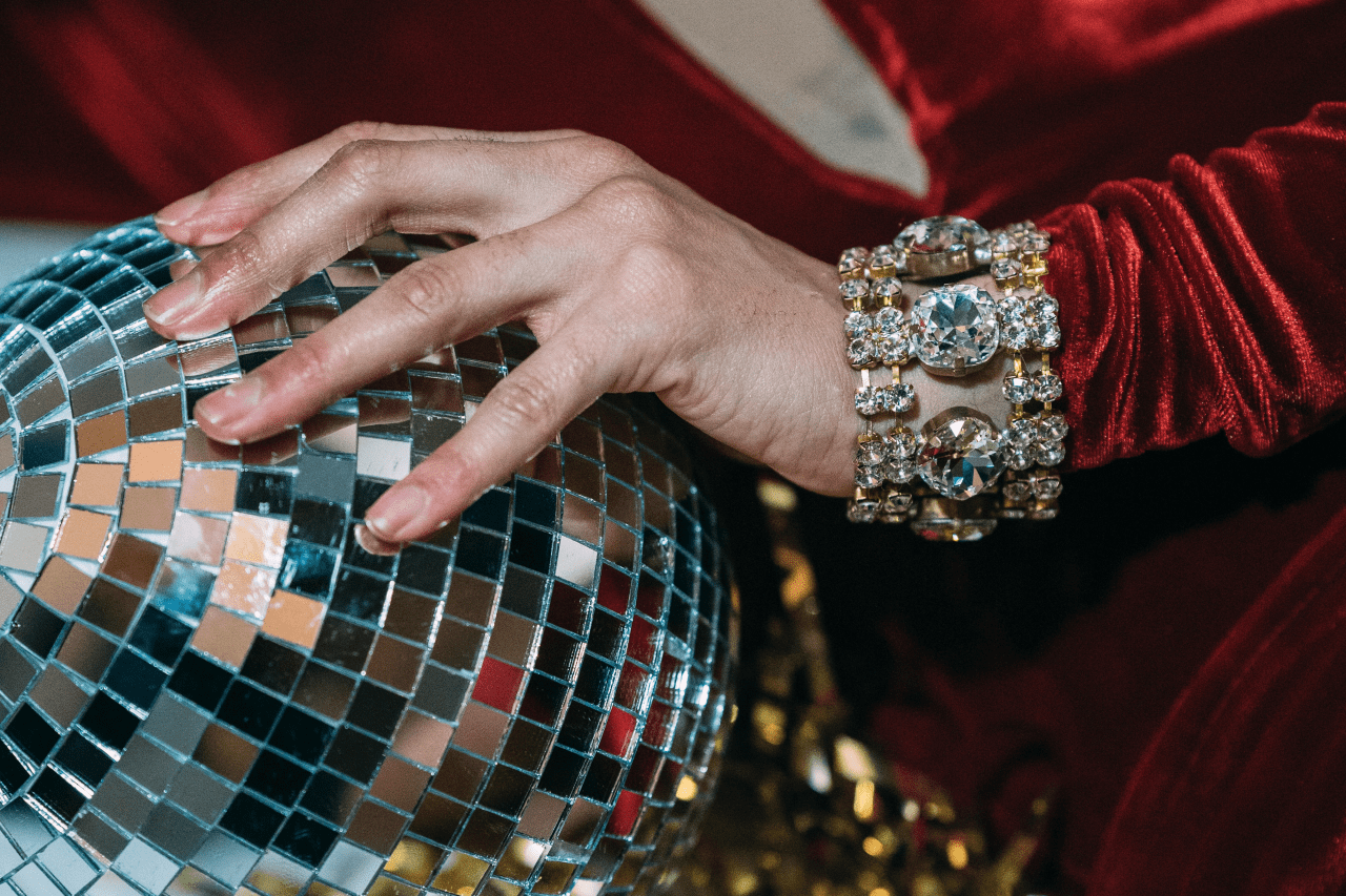 A woman’s hand resting on a disco ball and wearing a costume jewelry bracelet