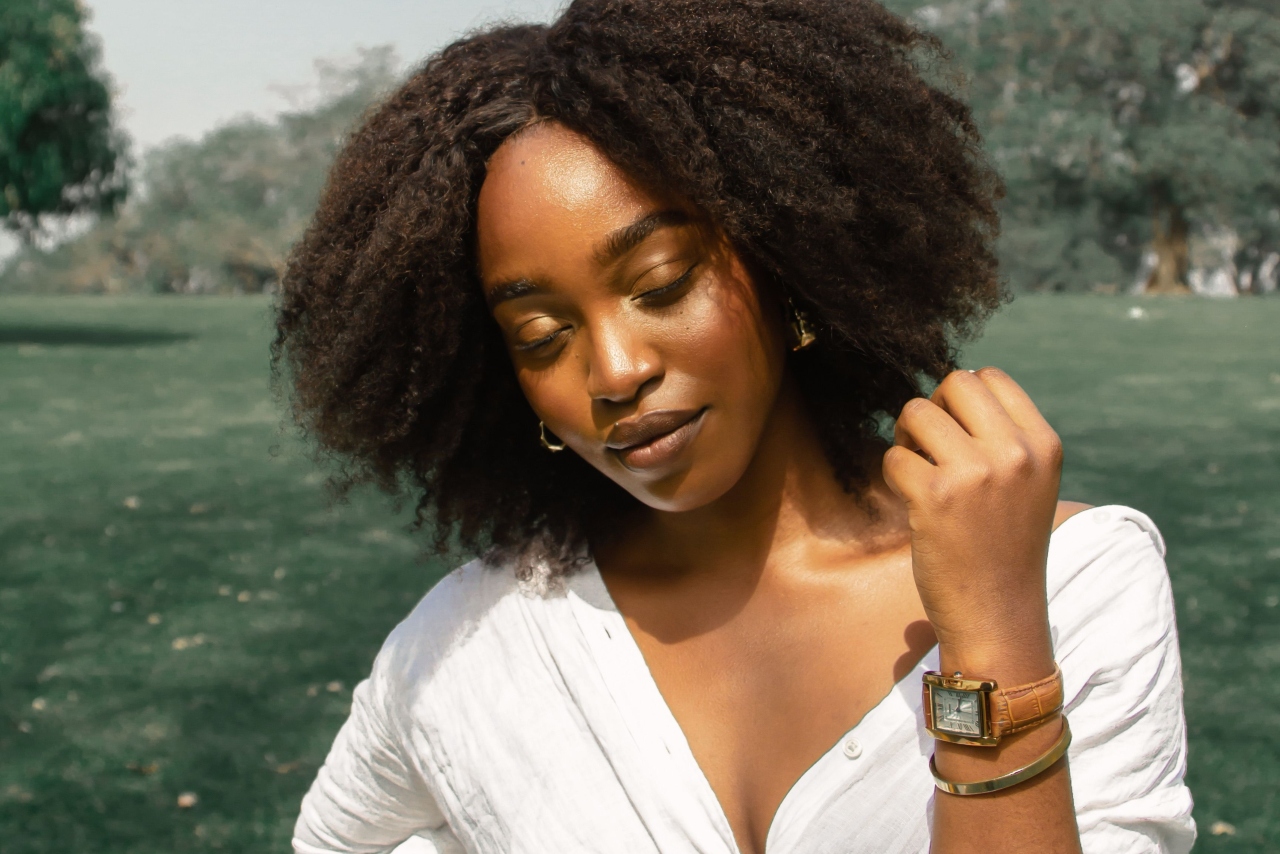 Curly-haired woman in a white shirt wearing a vintage watch in a park