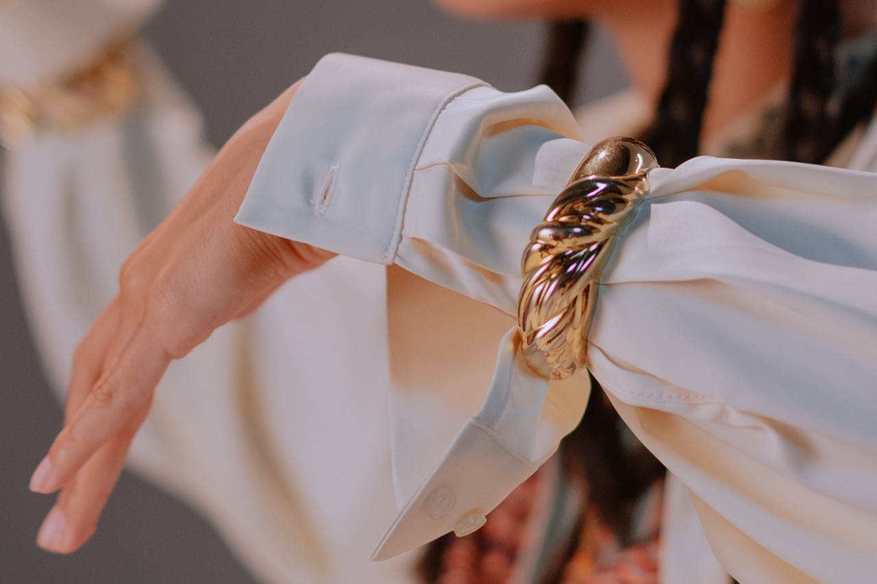 a woman’s arm wearing a white sleeve and a domed yellow gold bracelet.