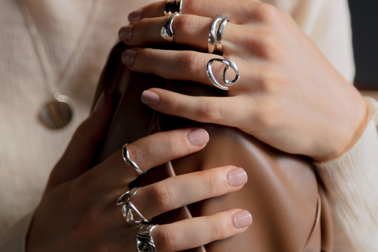 a woman’s hand resting on her knee, adorned with sculptural silver rings