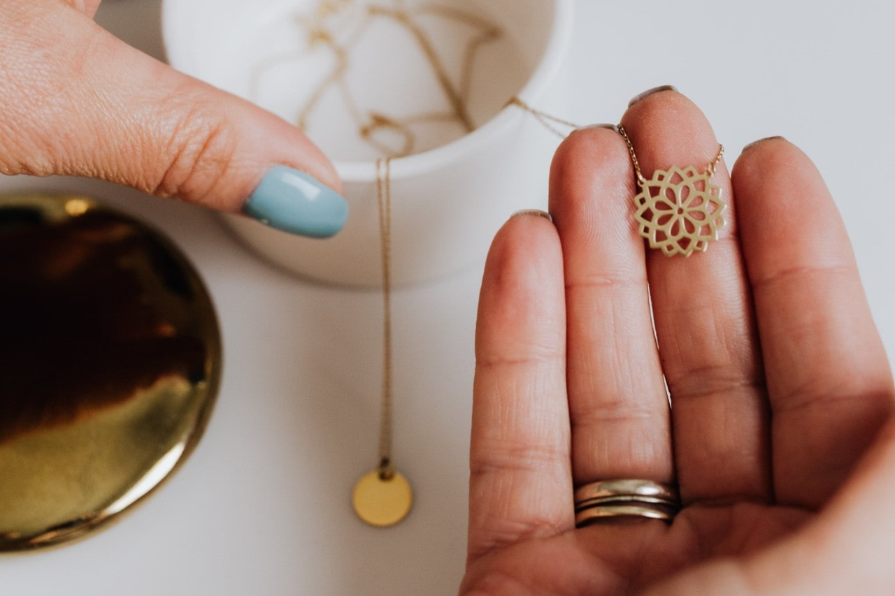 a woman’s hand holding a floral motif yellow gold pendant necklace