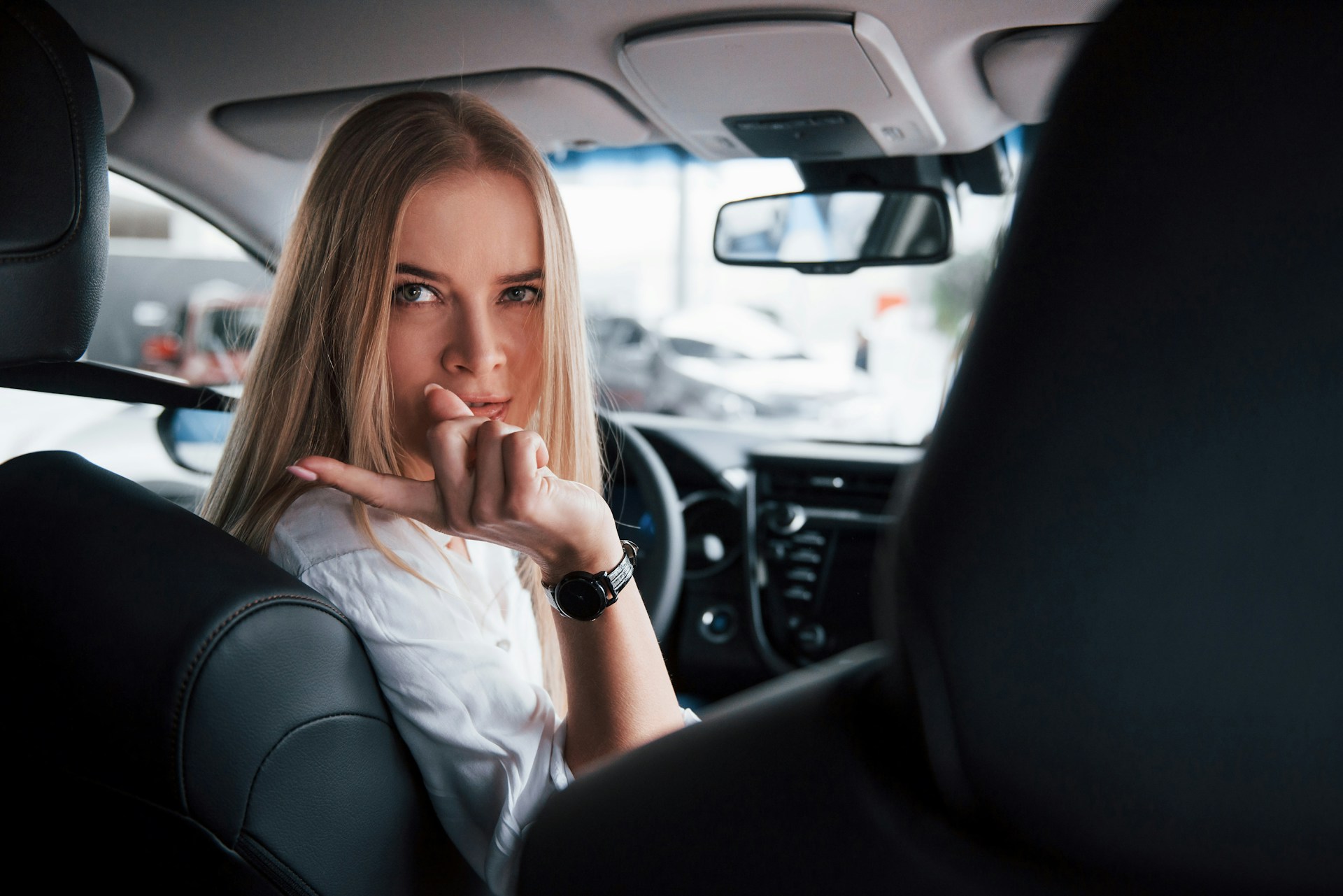 A woman in the driver’s seat of a car, wearing a luxury watch and pointing backwards.