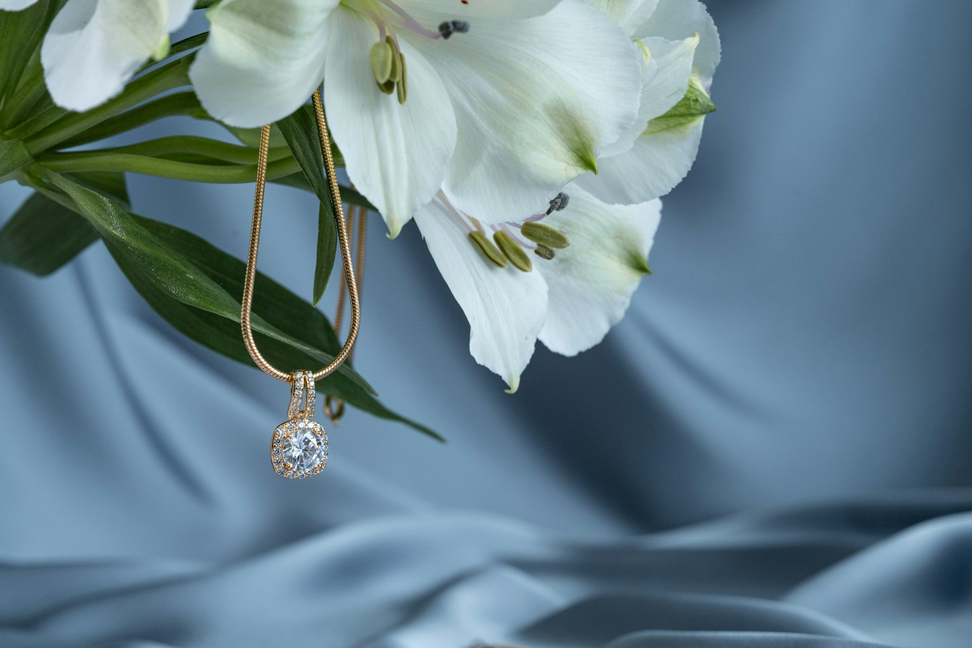 A close-up of a yellow gold and diamond pendant necklace draped from a pristine bunch of lilies.