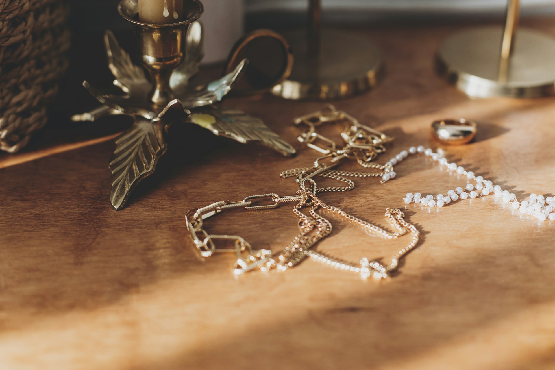 A close-up of three different necklaces and a gold ring displayed on a wooden table.