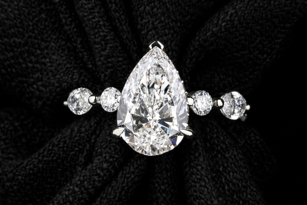 A close-up image of a white gold engagement ring with a pear shape center stone.