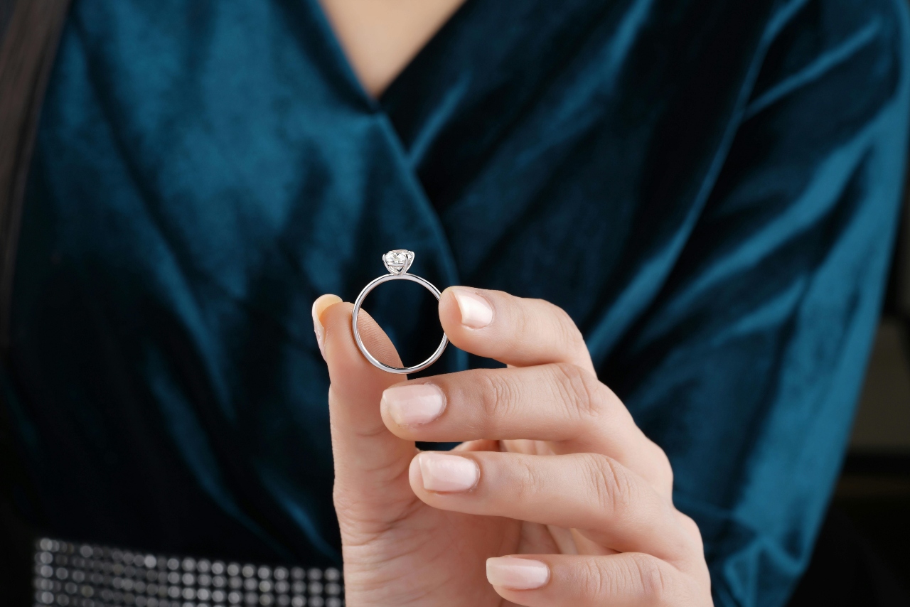 A close-up of a woman holding up a white gold solitaire diamond engagement ring.