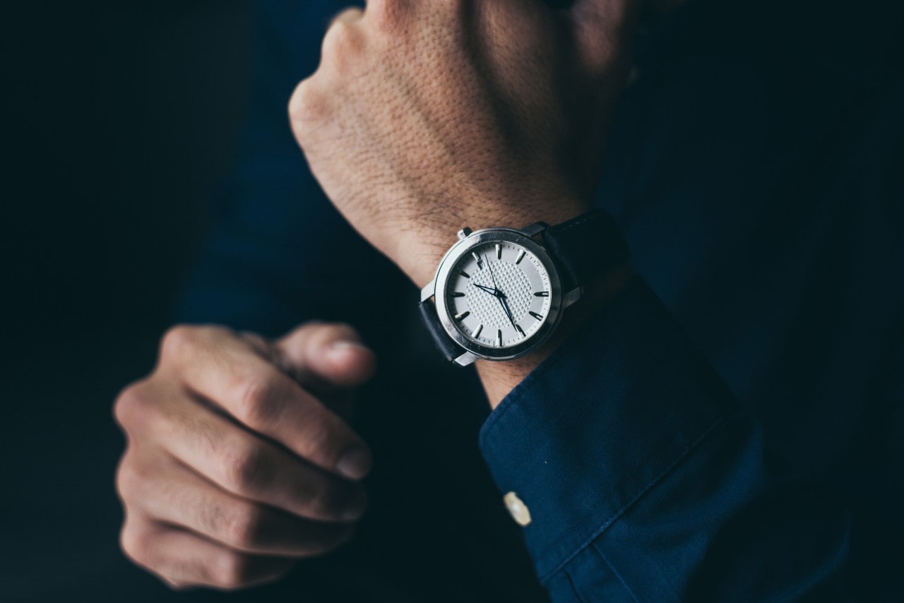 A silver and navy leather watch on the wrist of a man with a matching navy dress shirt