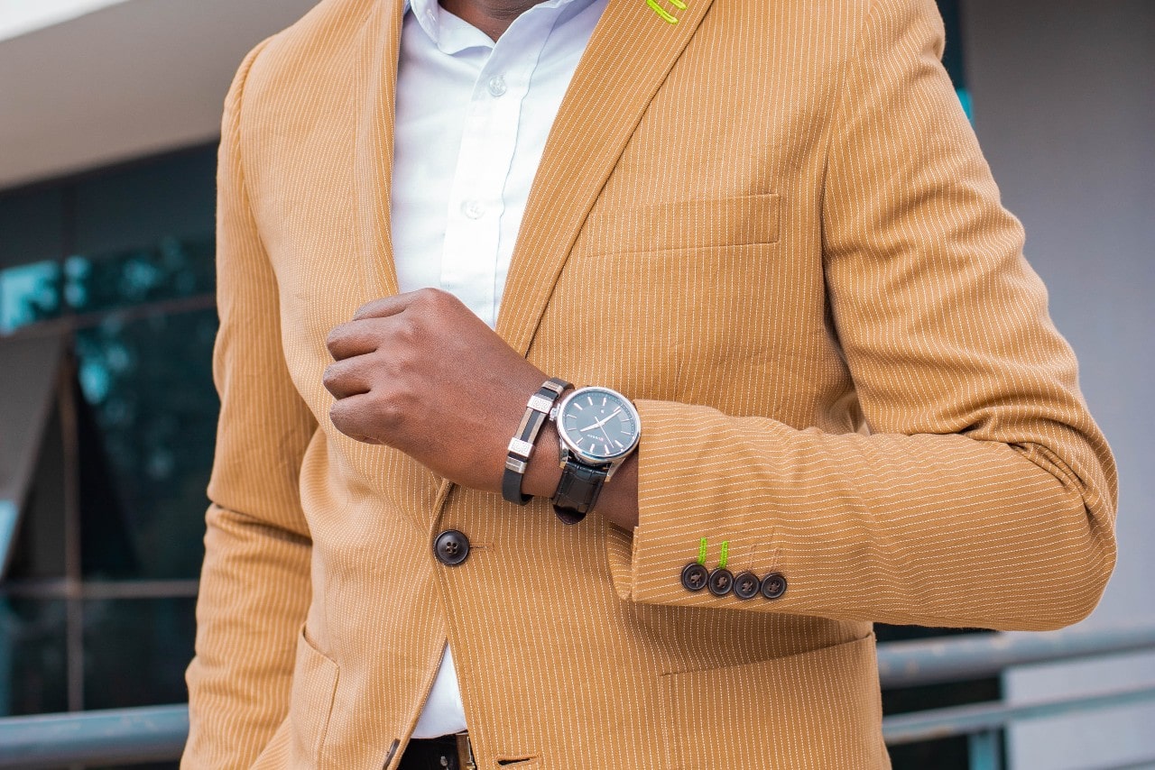 A man in a pinstripe marigold blazer, displaying a luxury watch.