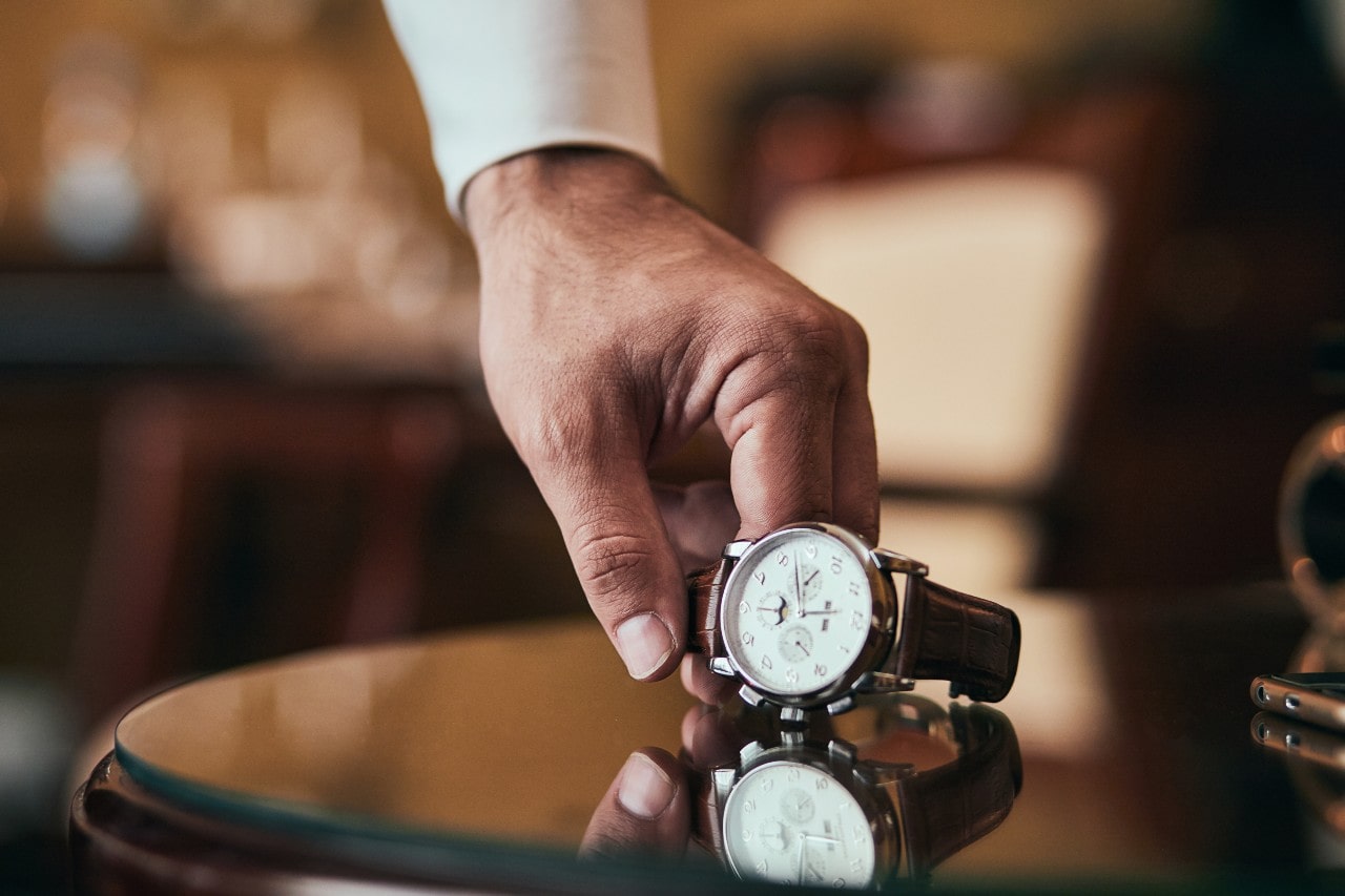 a man’s hand setting a luxury watch on a glass table