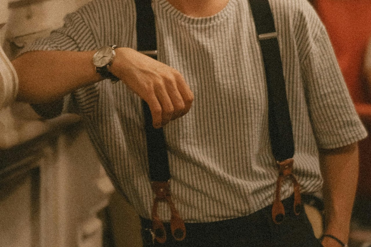 A close-up of a man leaning on a marble fireplace, wearing a luxury watch.